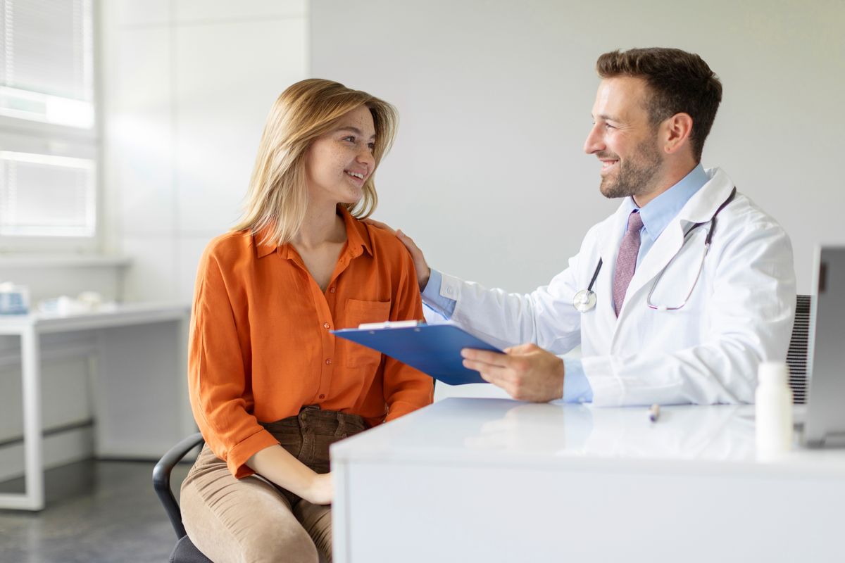 Young woman patient talking with male doctor during appointment in clinic office, free space