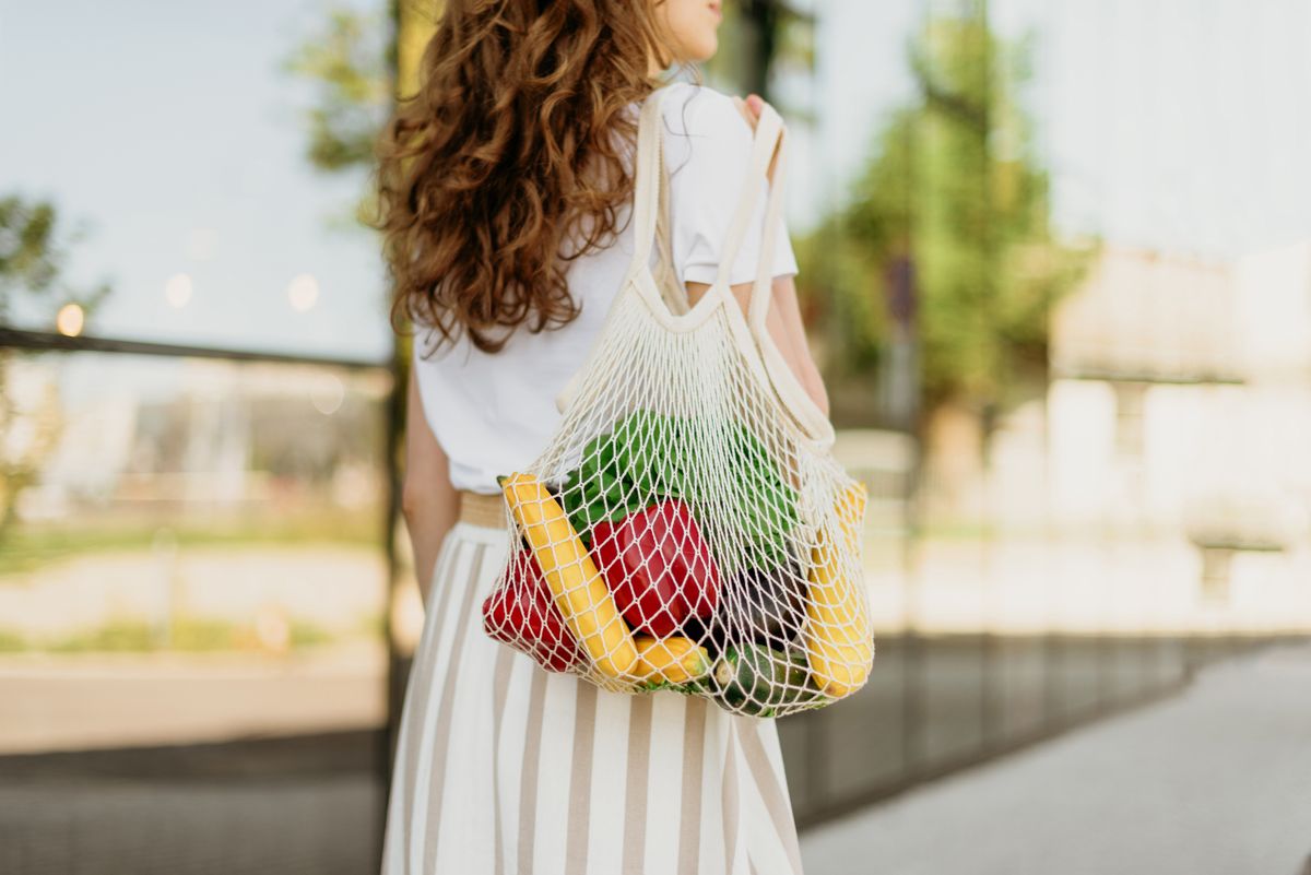 Zero waste concept with copy space. Woman holding cotton shopper and reusable mesh shopping bags with vegetables, products. Eco friendly mesh shopper. Zero waste, plastic free concept