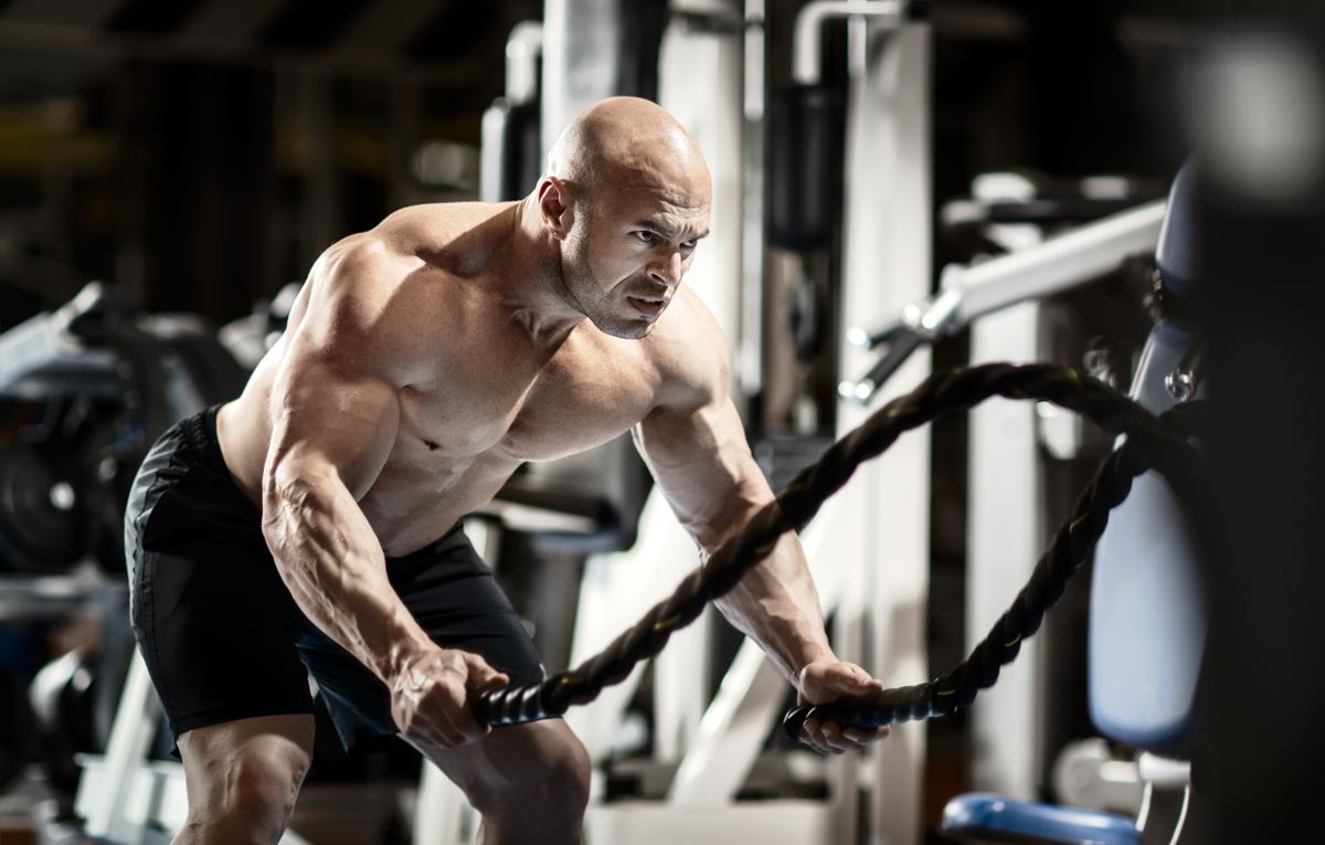 Man bodybuilder perform exercise with rope in GYM