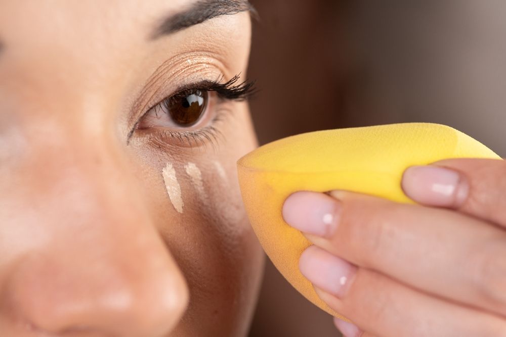 Close-up of Asian woman applying contouring makeup at home, using special sponge. Closeup