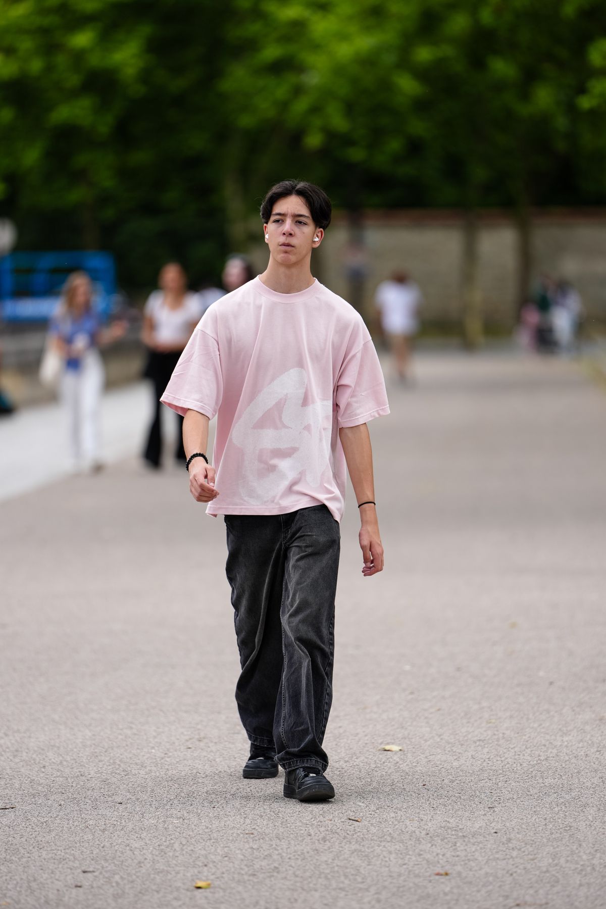 PARIS, FRANCE - JUNE 27: A guest wears a light pink oversized T-shirt featuring a large white graphic on the front. The T-shirt has a round neckline and short sleeves. Paired with the top are loose-fitting, dark gray jeans with a slightly faded texture. On the feet, black sneakers are visible. The hairstyle is short and parted in the middle. A black bracelet is worn on the right wrist, outside Dior, during Paris Fashion Week - Menswear Spring/Summer 2026, on June 27, 2025 in Paris, France (Photo by Edward Berthelot/Getty Images)