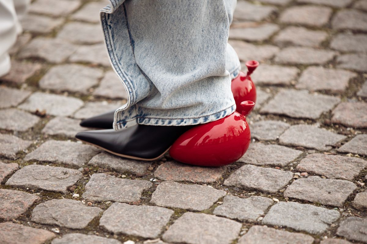 COPENHAGEN, DENMARK - FEBRUARY 01: Nina Sandbech wearing red sunglasses from Loewe, silver large earrings, a silver chain with a flower pendant necklace, a red cutout body, a red cropped puffer jacket, a red shiny leather zipper handbag in the shape of heart, blue faded jeans, black shiny leather pointed shoes from Loewe with the heel as balloon imitation outside OperaSport, during the Copenhagen Fashion Week Autumn/Winter 2023 on February 01, 2023 in Copenhagen, Denmark. (Photo by Raimonda Kulikauskiene/Getty Images)