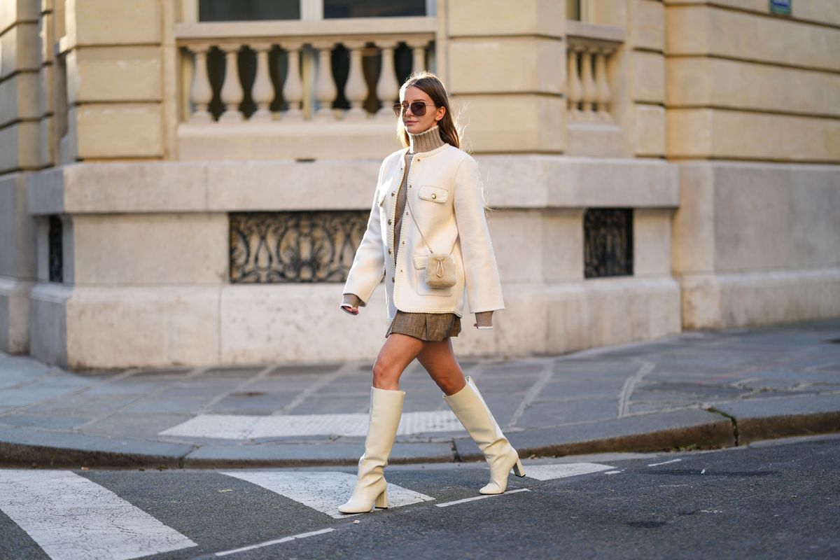 PARIS, FRANCE - JANUARY 13: Diane Batoukina wears brown Dior sunglasses, a brown Sandro turtleneck pullover, a white wool Sandra jacket, a light brown fluffy faux fur Prada bag, a brown Sandro mini skirt, white leather Zara boots high heels, during a street style fashion photo session, on January 13, 2025 in Paris, France. (Photo by Edward Berthelot/Getty Images)