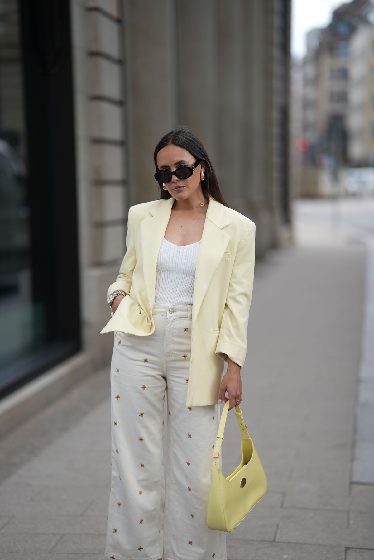 HAMBURG, GERMANY - MAY 5: Laura Noltemeyer is seen wearing a butter yellow blazer from Zara, a knitted v-neck top in viscose crêpe in white from Drykorn, a 5-pocket wide-leg jeans with all-over small flower embroidery in ecru from Sézane x Lucia Vergara, a pale yellow shoulder bag with small golden details from Marc Cain, black TRIOMPHE sunglasses with round glasses and golden logo detail on temples from Celine, golden drop earrings, golden Love bracelets from Cartier, stacked rings from Cartier, small silver-golden Datejust watch from Rolex on May 5, 2025 in Hamburg, Germany. (Photo by Moritz Scholz/Getty Images)