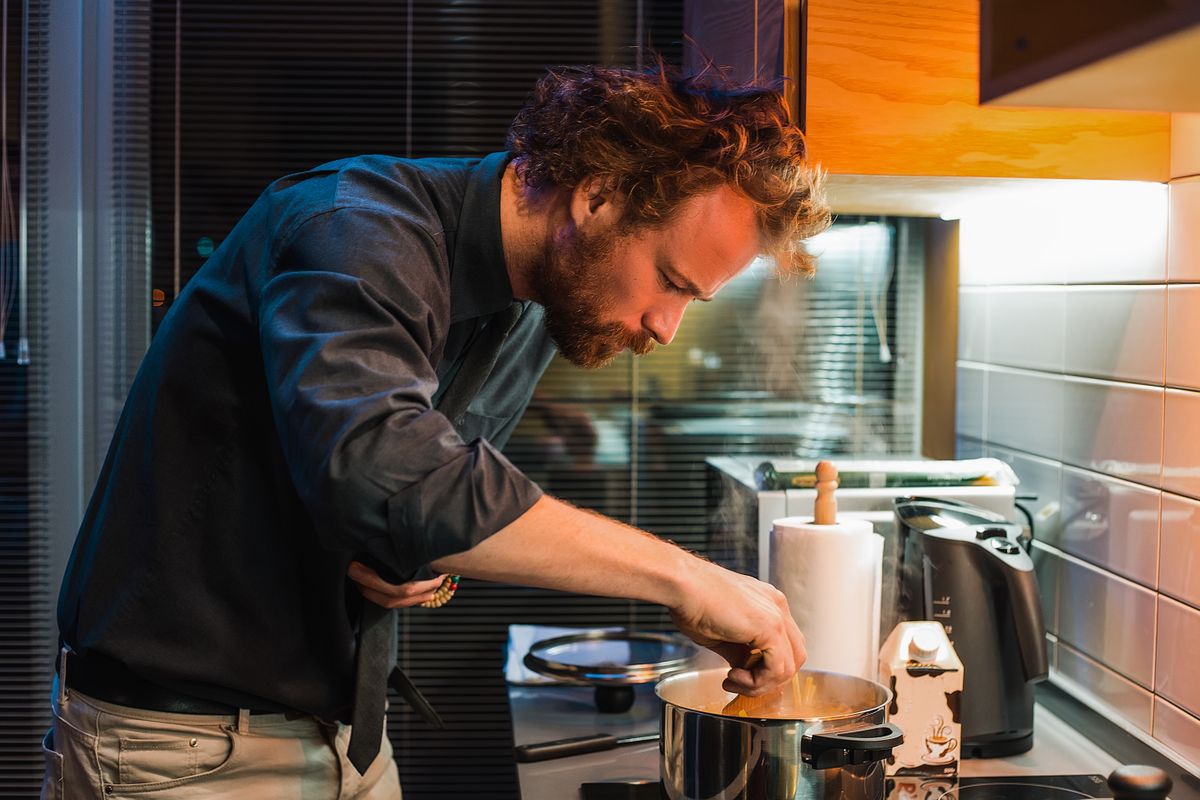Handsome man cooking at the kitchen, man curly hair style, man in black shirt, bearded man, home party, prepare dinner, pan, pasta, kettle, delicious, food, evening, pretty, seriously, concentration