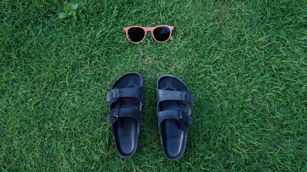 Flat lay summer fashion accessories concept of sunglasses and sandals shoes on green grass background, vacation and summertime background