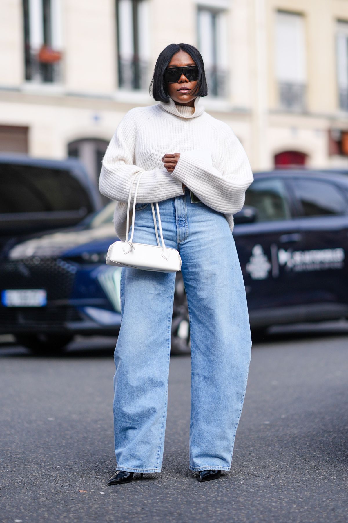 PARIS, FRANCE - FEBRUARY 28: A guest wears a white oversized turtleneck ribbed wool pullover, sunglasses, blue denim wide-leg jeans / pants, white leather bag, black leather pointed shoes, outside Undercover, during the Womenswear Fall/Winter 2024/2025 as part of  Paris Fashion Week on February 28, 2024 in Paris, France. (Photo by Edward Berthelot/Getty Images)