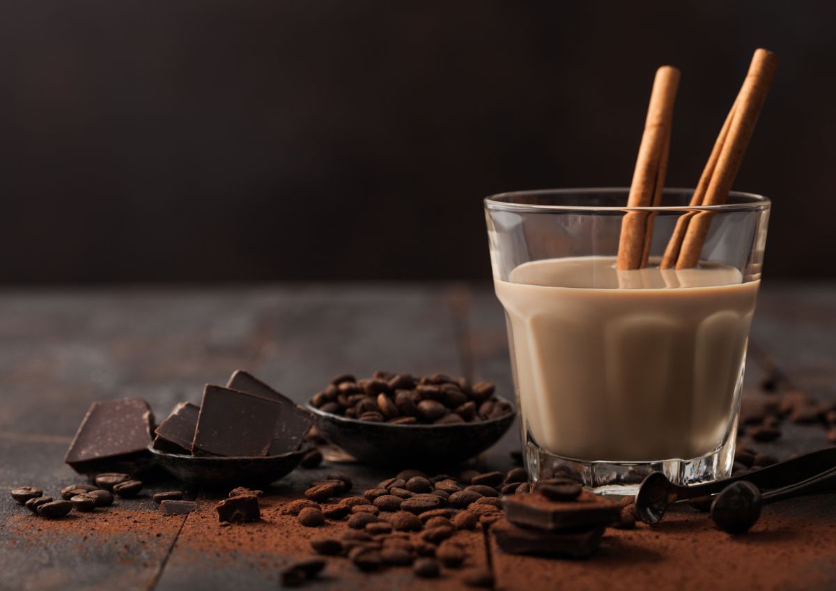 Crystal glass of Irish cream baileys liqueur with cinnamon, coffee beans and powder with dark chocolate on dark wood background. Space for text