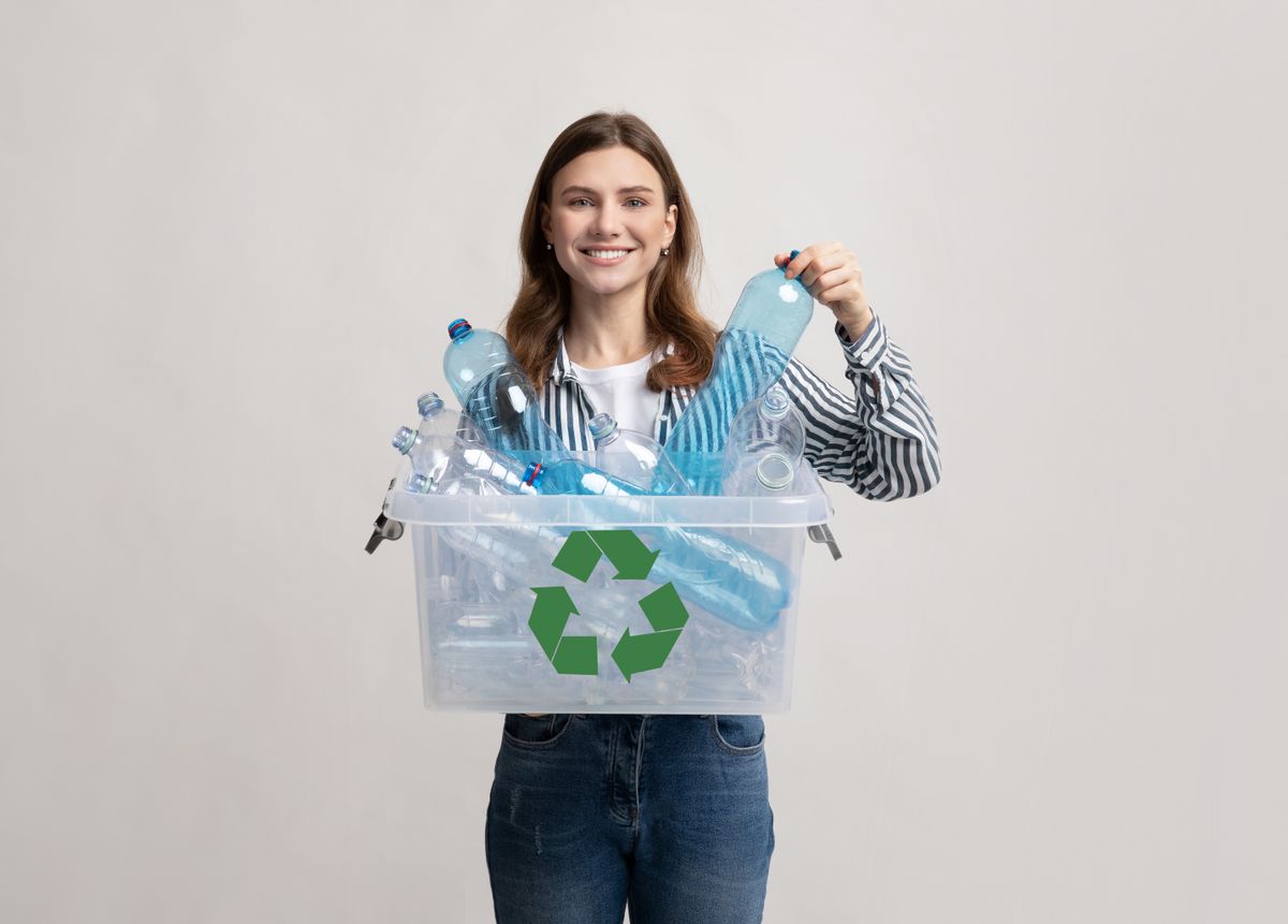 Waste For Recycling. Cheerful Young Woman Carrying Container Box With Empty Plastic Bottles, Positive Millennial Female Sorting Garbage, Enjoying Zero Waste Living, Standing On Grey Studio Background