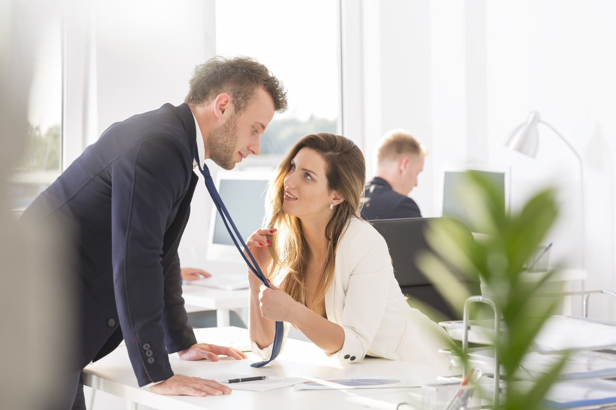 Woman grabbing man's tie and flirting at work