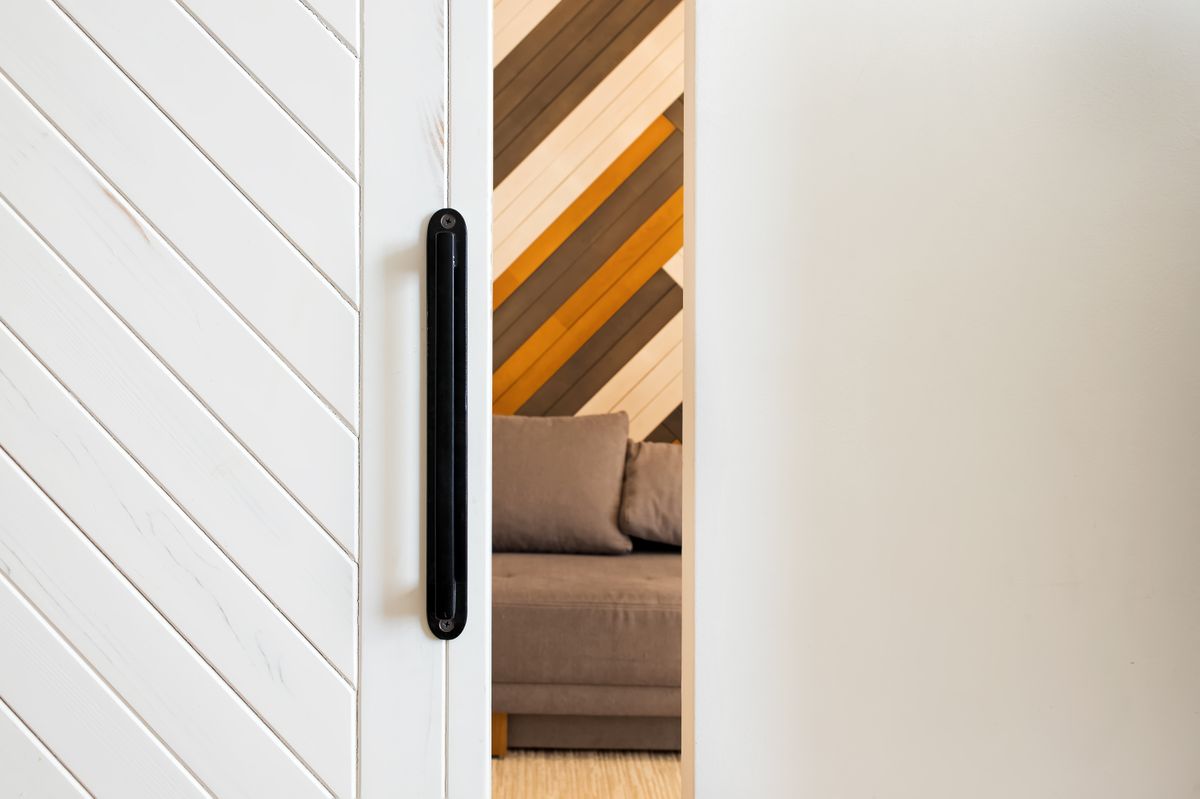 Small gap between white wooden sliding door and wall with room on the background