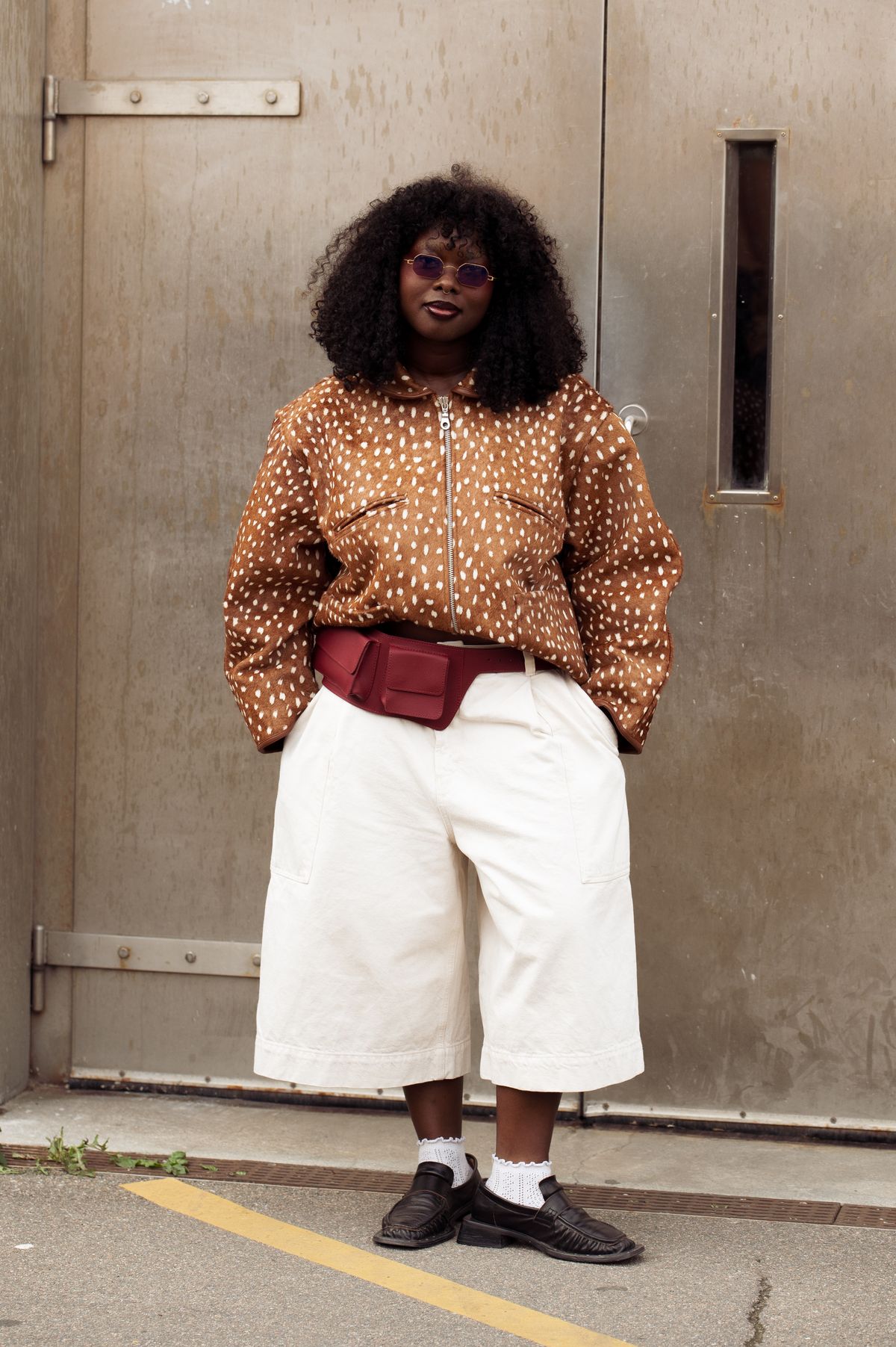 COPENHAGEN, DENMARK - AUGUST 04: A guest wears white wide long shorts, white socks, brown loafers, burgundy belt bag, brown fur jacket with white dots outside Bonnetje show during Copenhagen Fashion Week day one on August 04, 2025 in Copenhagen, Denmark. (Photo by Raimonda Kulikauskiene/Getty Images)