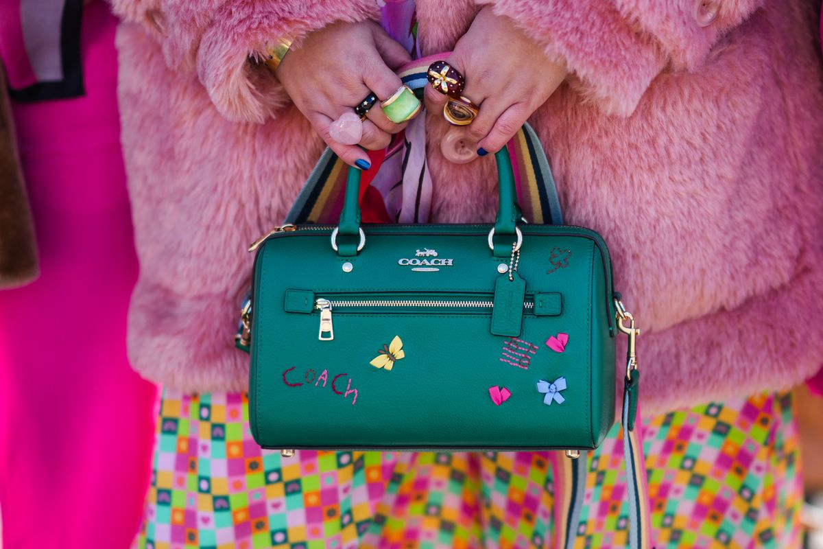 NEW YORK, NEW YORK - FEBRUARY 14: Greivy Lou wears a pale orange fluffy oversized winter coat, a pale pink / green / neon yellow / orange checkered print pattern dress, large gold and green rings, a dark green shiny leather handbag with embroidered pins from Coach, outside the Coach show, during New York Fashion Week, on February 14, 2022 in New York City. (Photo by Edward Berthelot/Getty Images)