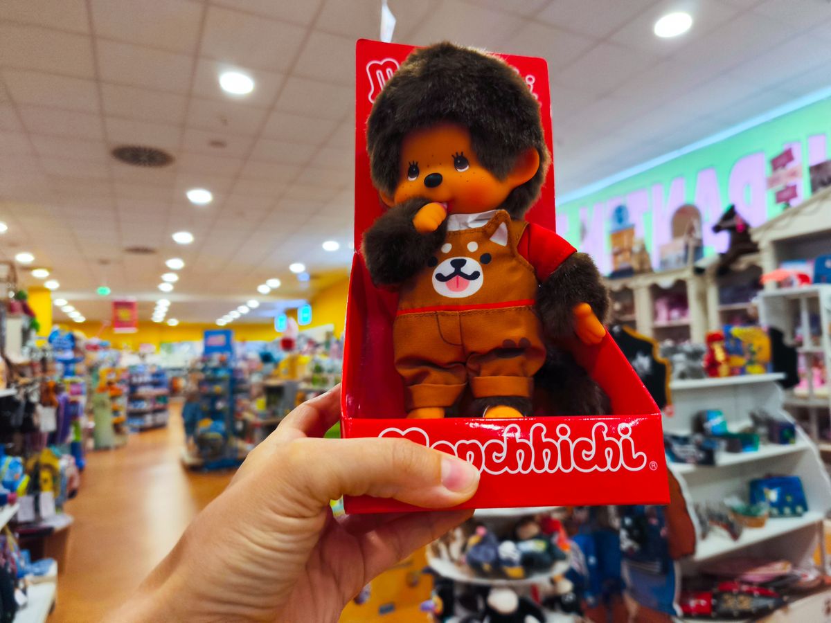 Potsdam, Germany - September 04, 2025: Hand is holding a Monchhichi doll in a bright toy store filled with shelves of various toys and colorful displays