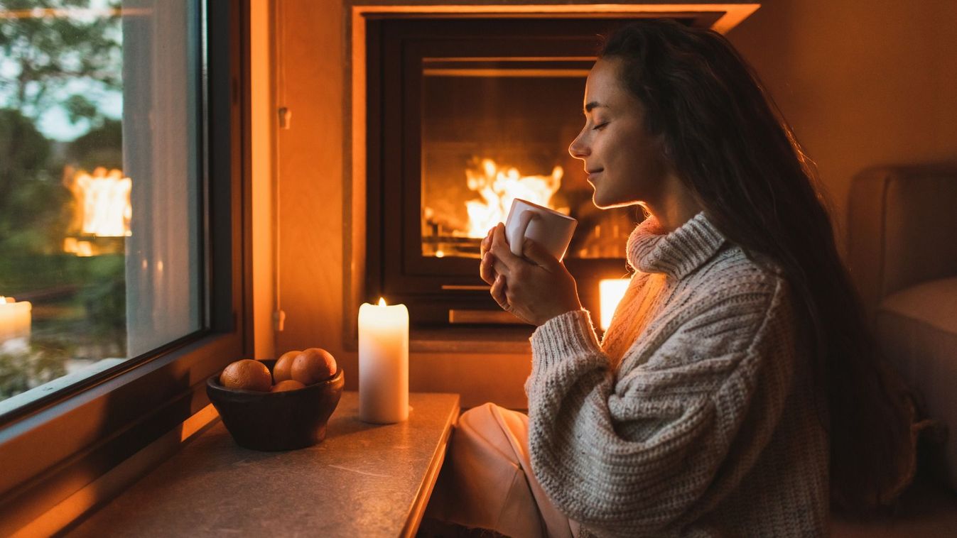 gyönyörű nő ül és szürcsöli a forró teát a kandalló előtt