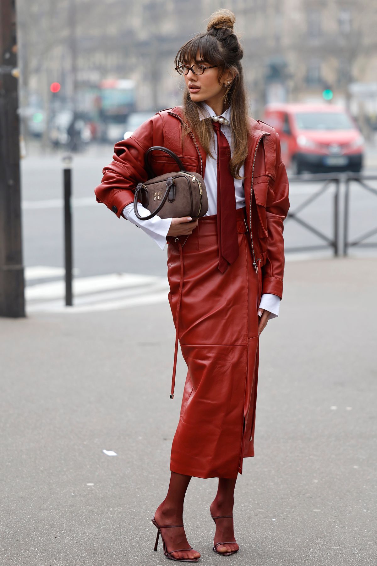 PARIS, FRANCE - MARCH 11: A guest wears white shirt, red tie, red leather jacket with matching pencil skirt, brown Miu Miu bag, red tights, burgundy heels, outside Miu Miu, during the Womenswear Fall/Winter 2025/2026 as part of Paris Fashion Week on March 11, 2025 in Paris, France. (Photo by Claudio Lavenia/Getty Images)