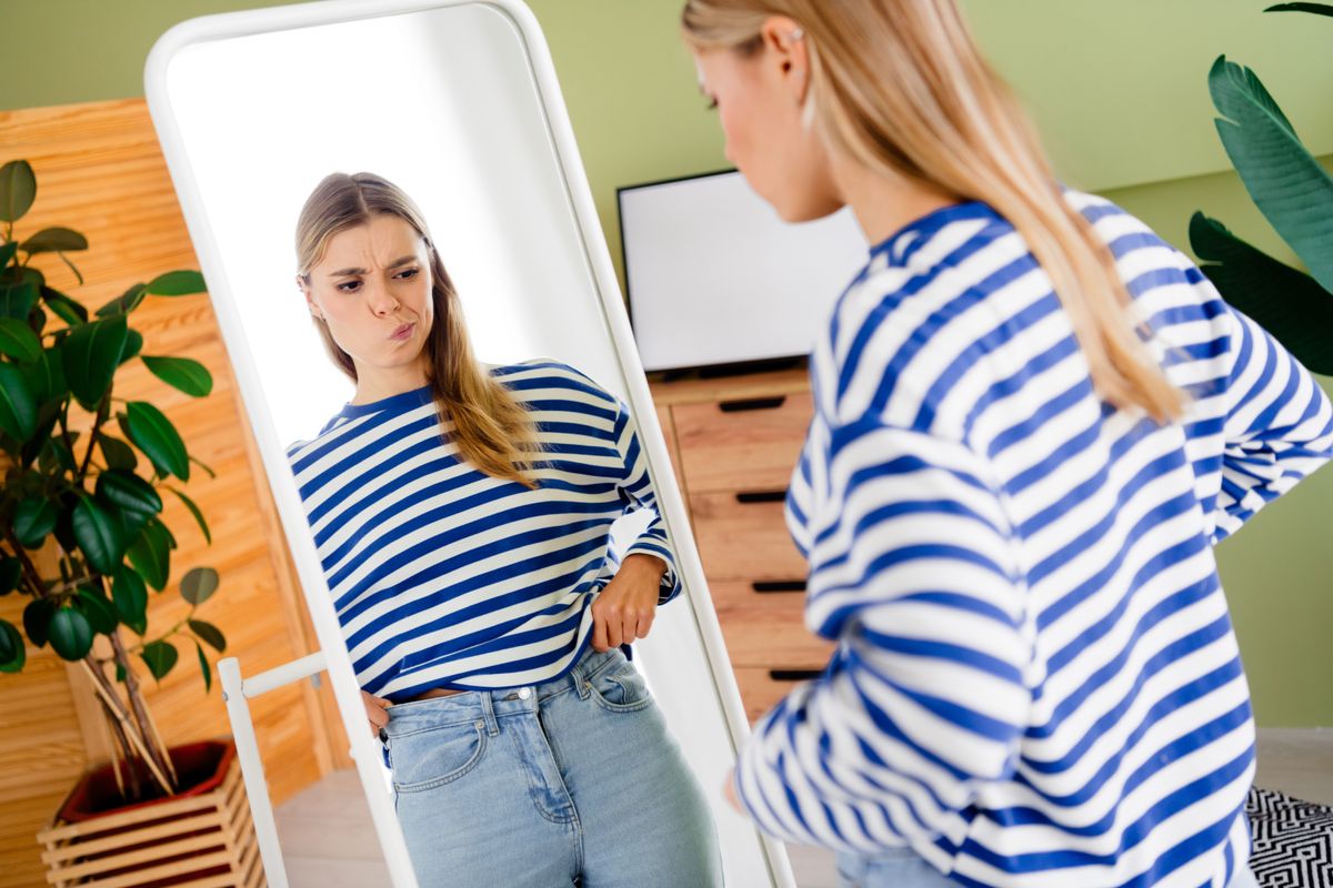 Fiatal nő a tükör előtt elégedetlen a testével az étkezése miatt