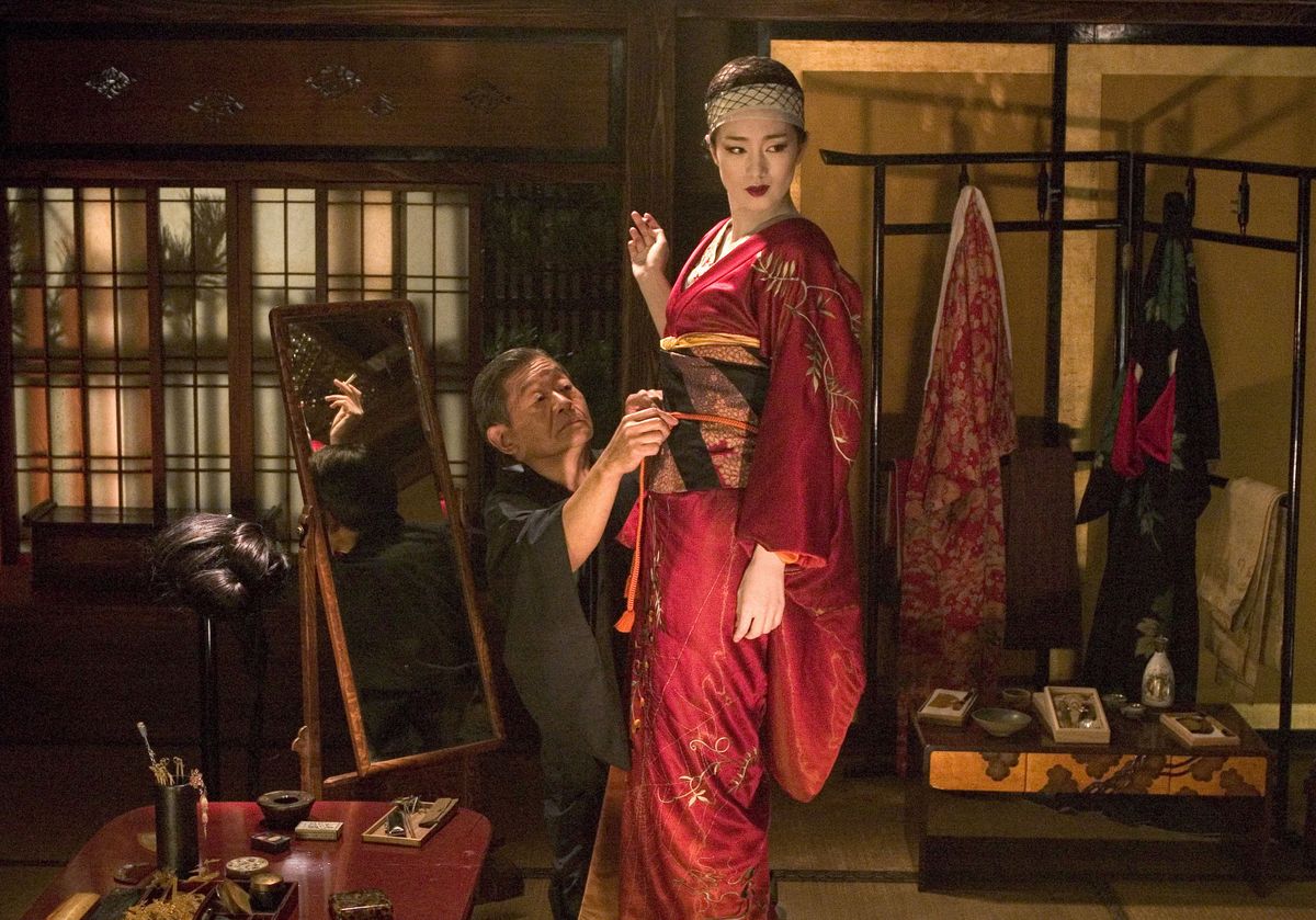 Filmjelenet, amiben egy gésát öltöztetnek. 