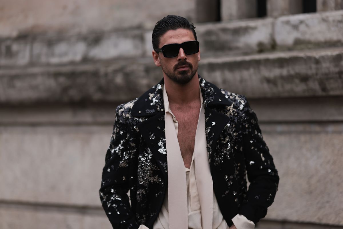 PARIS, FRANCE - MARCH 04: Michele Morrone wears Dolce & Gabbana black sunglasses, a black sequin suit jacket, a beige satin shirt with a scarf detail, black pants and a black leather belt, outside Elie Saab show, during Paris Fashion Week on March 04, 2023 in Paris, France. (Photo by Jeremy Moeller/Getty Images)
