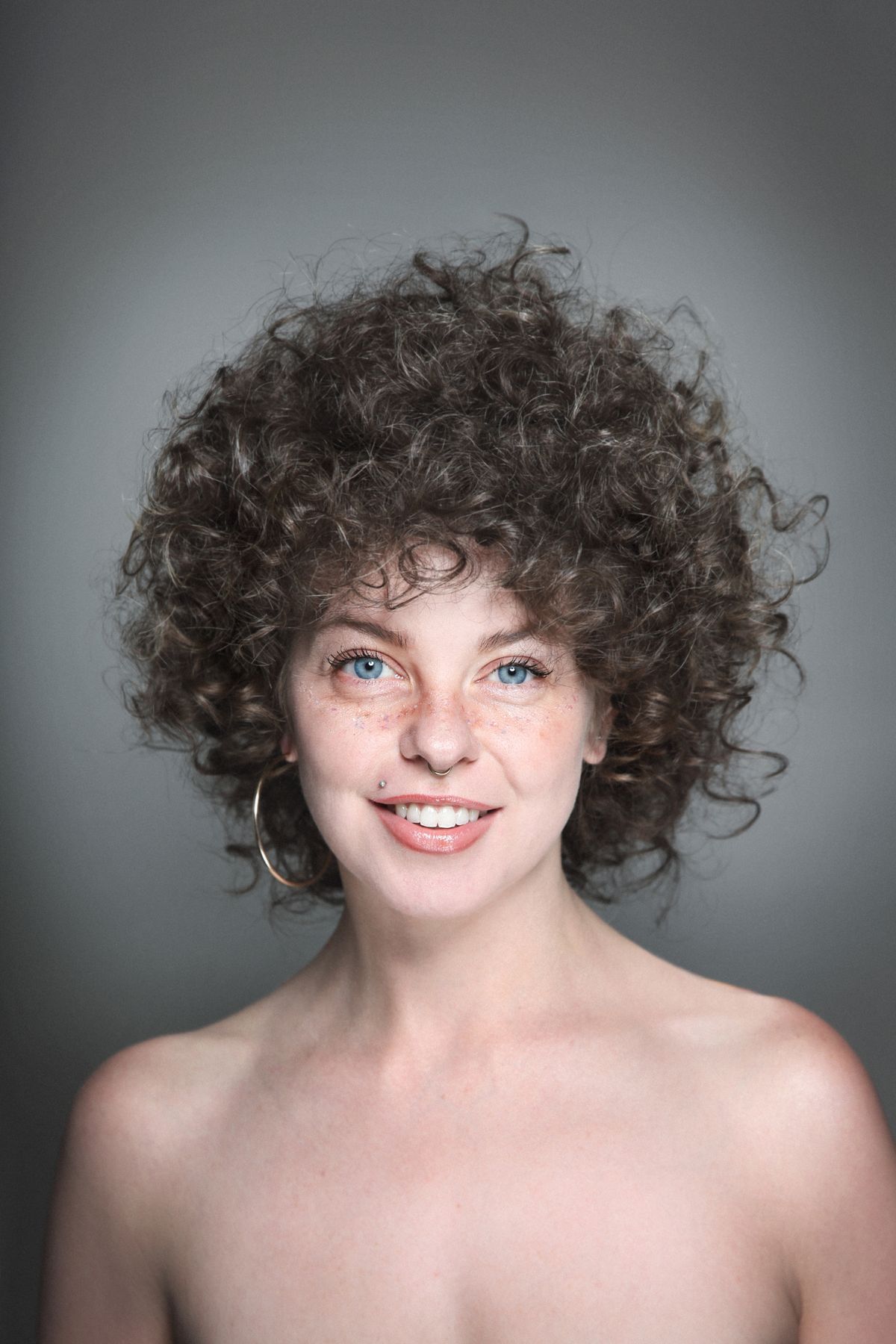 Portrait of young beautiful smiling woman with curly hair, false freckles and piercing