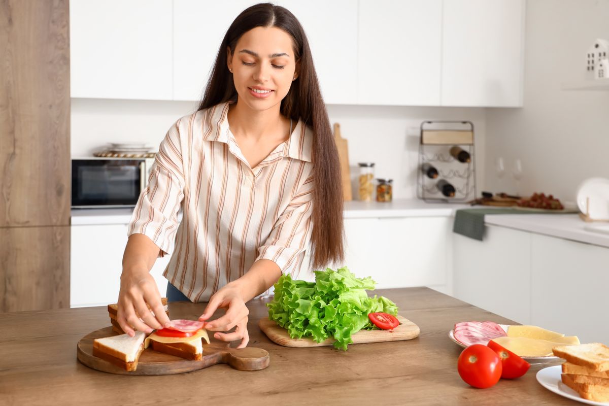 Young woman making tasty sandwich in kitchen
