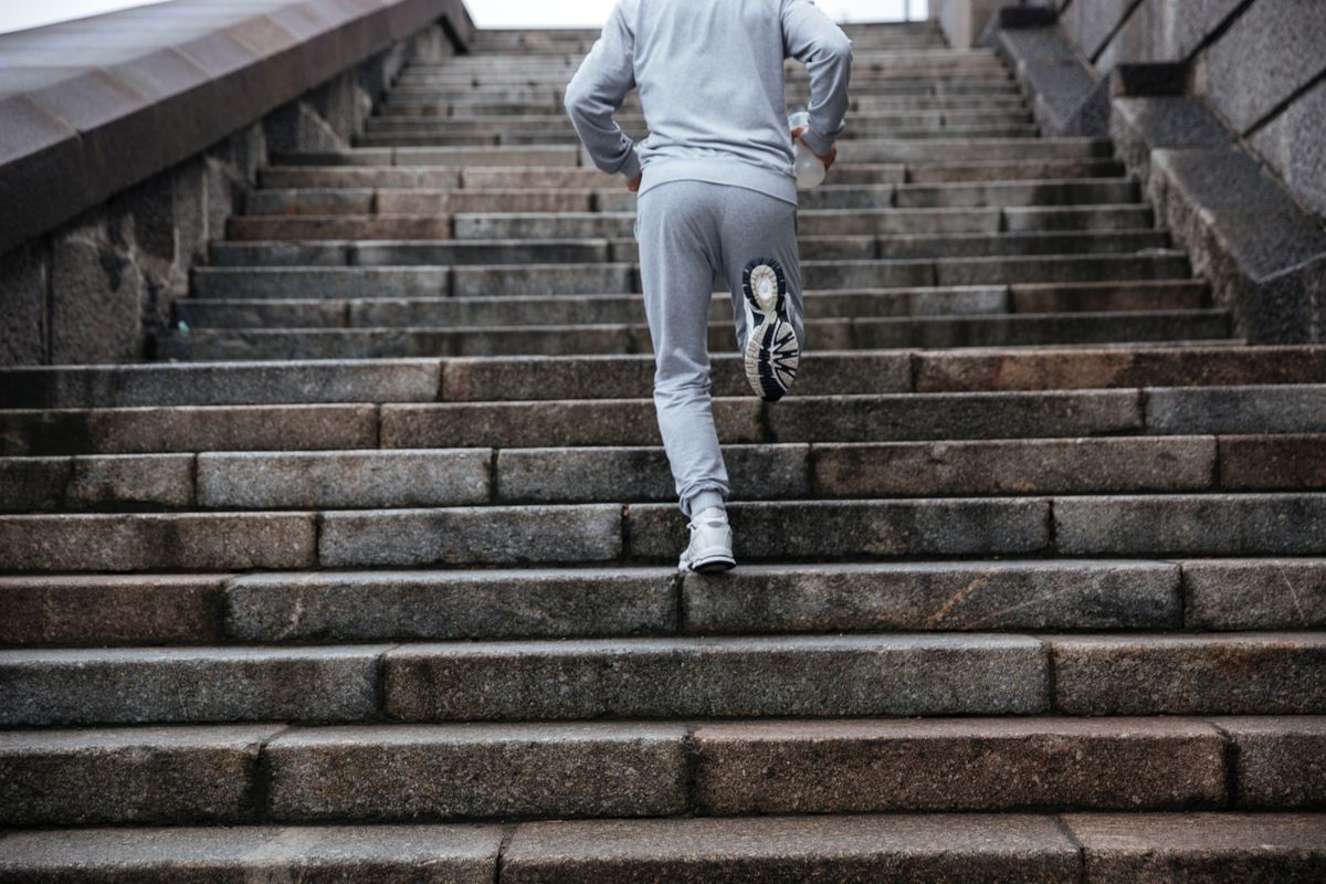Back view of man in gray sportswear running on stairs. Cropped image