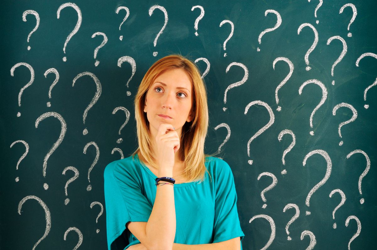 Egy nő gondolkozik a szólások és közmondások jelentésein egy kérdőjelekkel teli tábla előtt.