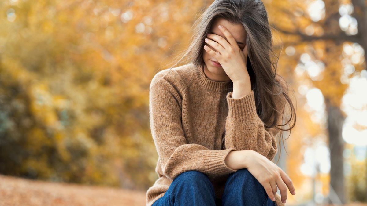 Closeup faceless upset woman has mental health problems. Melancholic girl covered her face with her hands sitting on the steps in the autumn park. Autumn depression, melancholy and blues. Copy space.