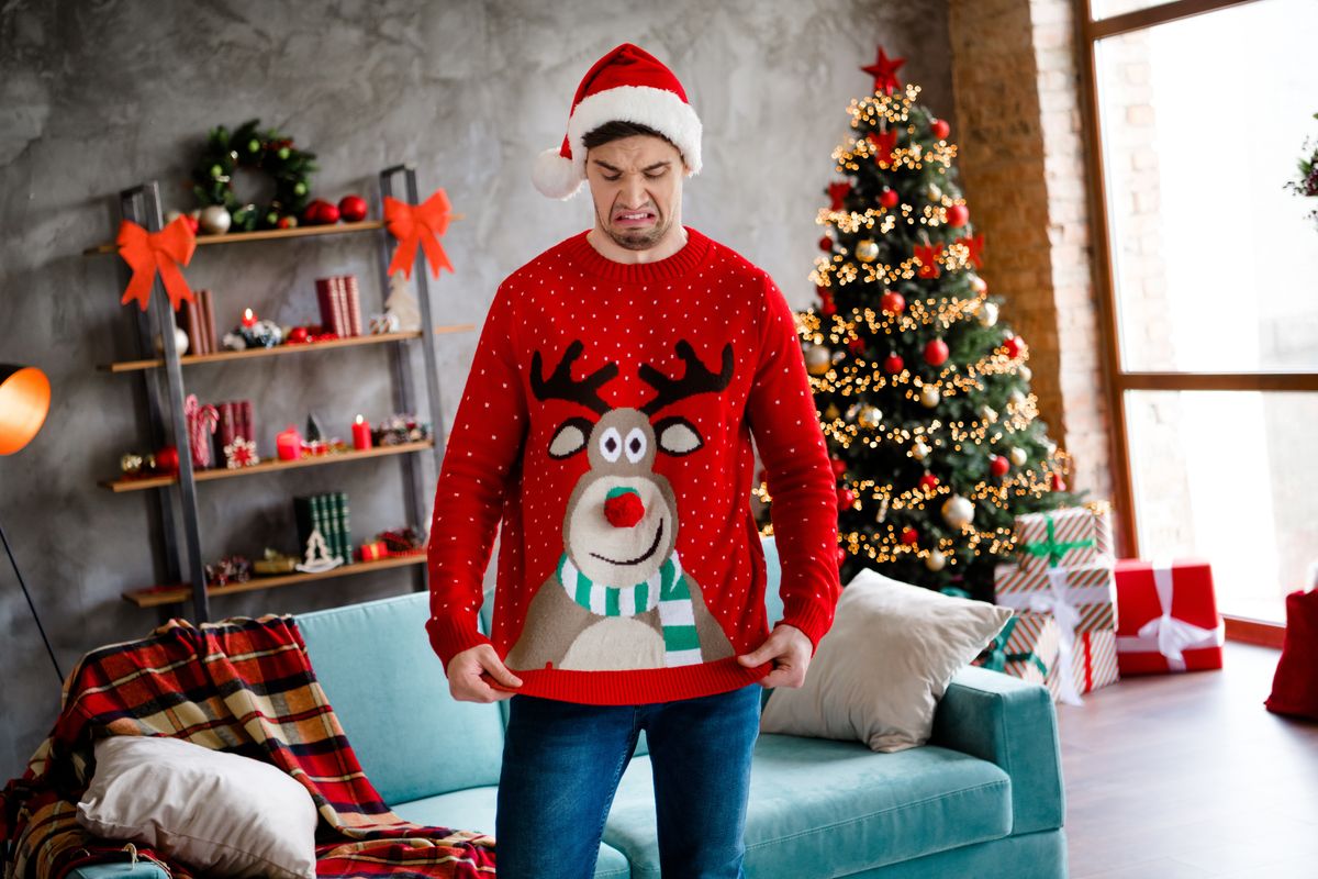 Fiatal férfi karácsonyi pulcsiban ronda karácsonyfa előtt