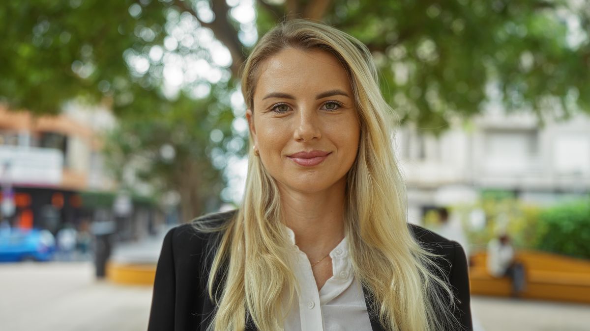Woman standing confidently in an urban park setting, embodying beauty and positivity, surrounded by city life and greenery, wearing business attire, representing professional elegance.