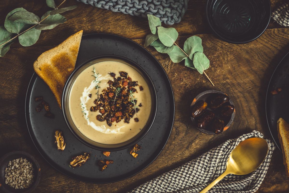 Bowl of chestnut soup with rosted topping, cream and bread in a black bowl on rustic wooden background, top view