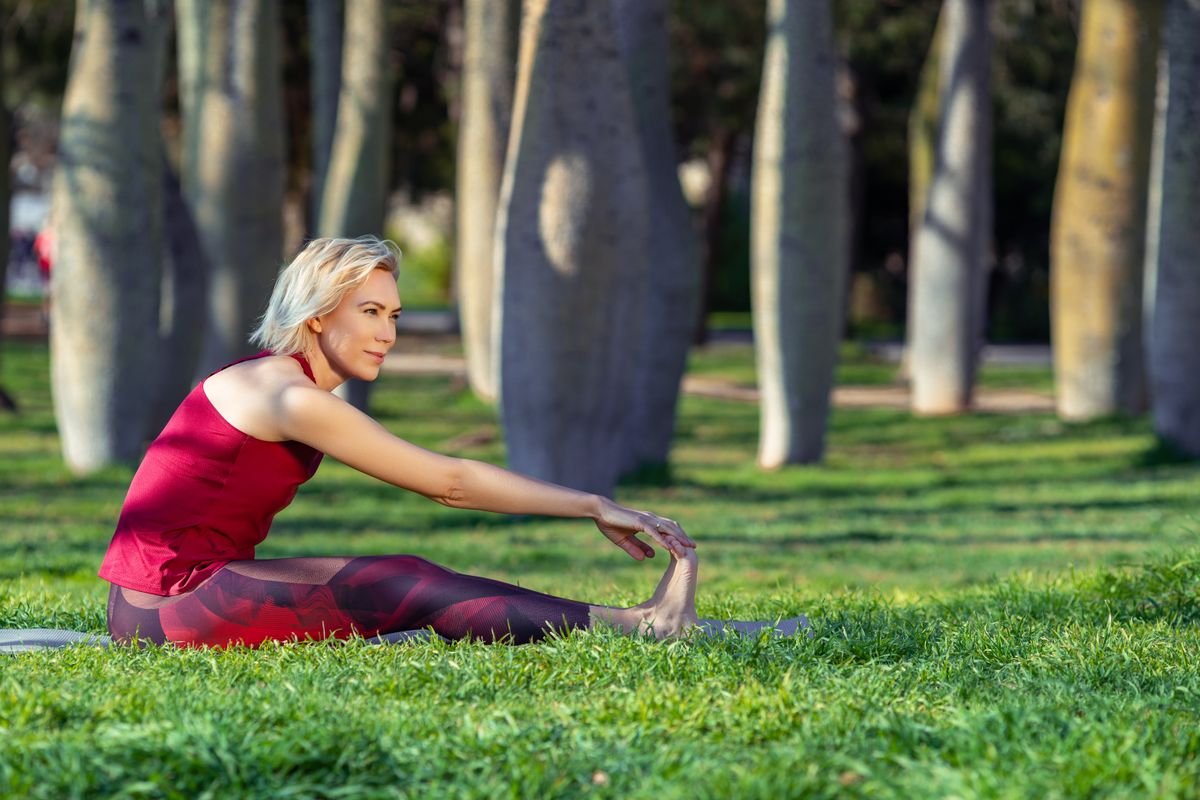 Állóképesség teszt: te eléred lábujjaid? A képen lévő, szőke hajú, piros ruhás, természet lágyölén jógázó nő meg tudja csinálni.?