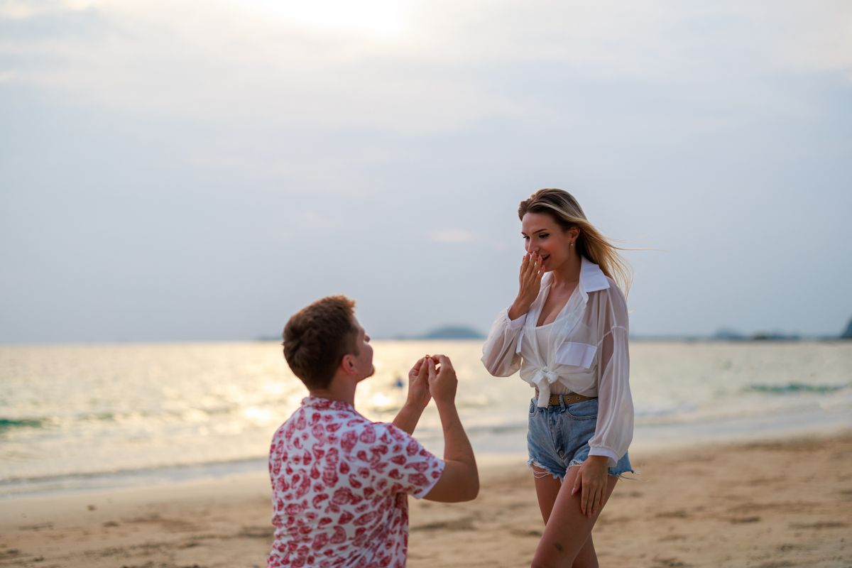 Lánykérés, egy férfi megkéri a nő kezét a tengerparton. 