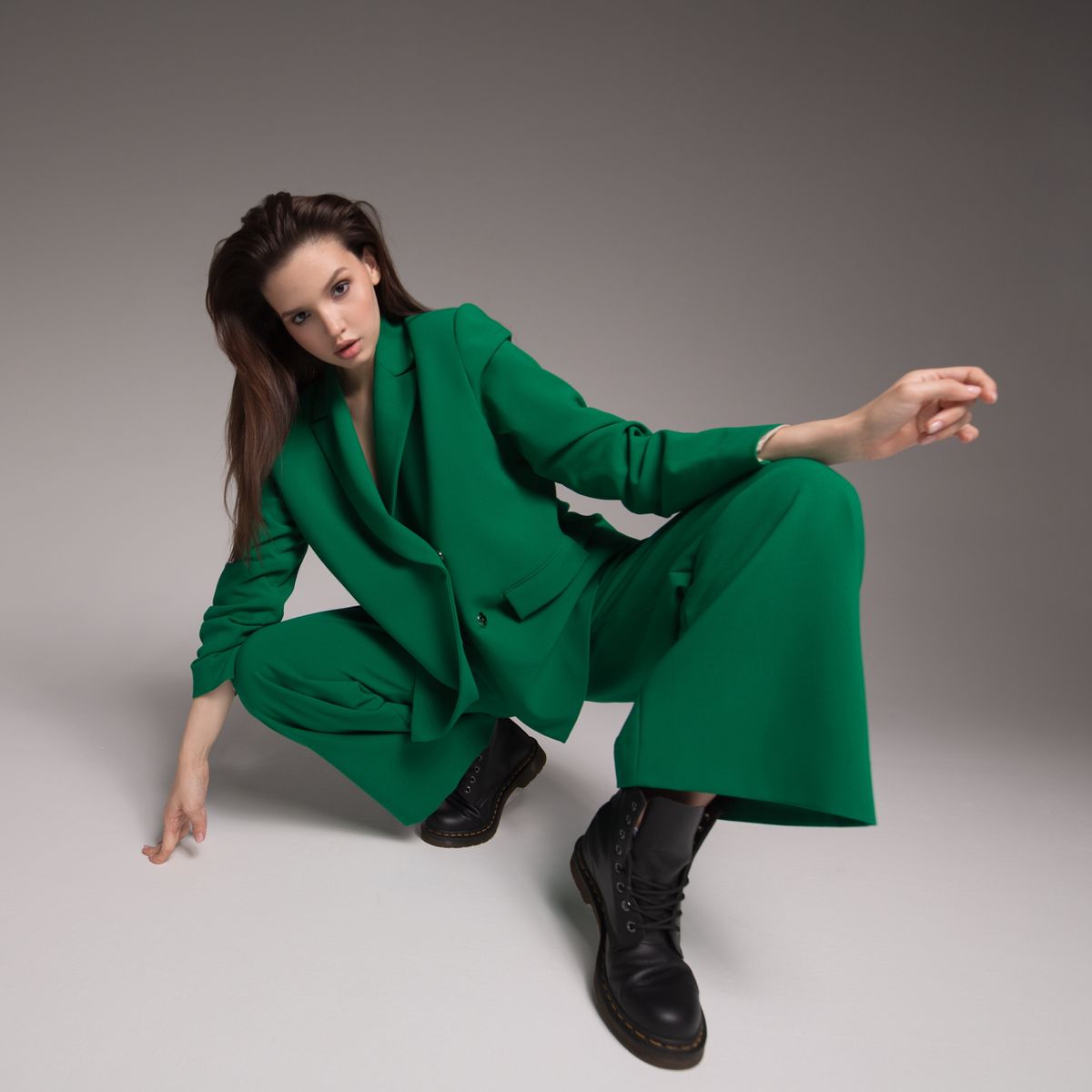 Fashion portrait of a charming girl dressed in a green suit. Gray background.