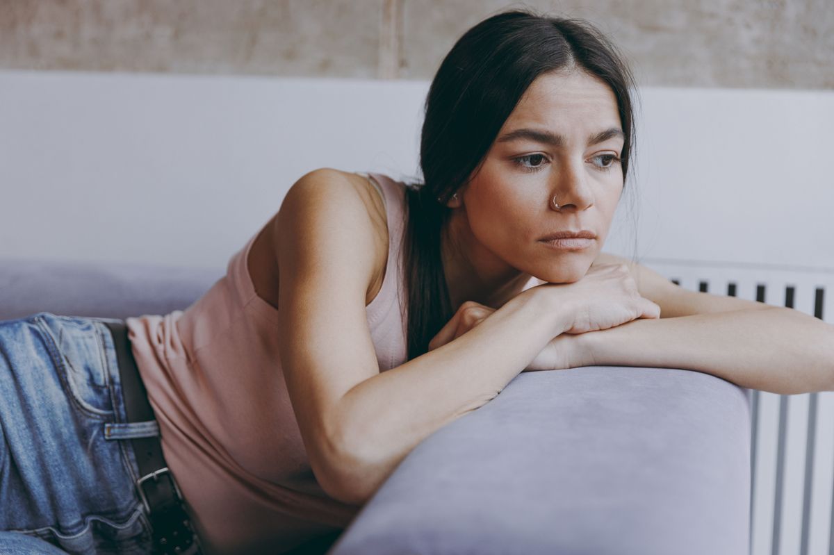 : A mérgező szülők nyoma nem tűnik el a felnőttkor küszöbén – csak megtanuljuk másképp hordozni. - Unnerved sad worried minded young latin woman 20s in casual clothes sit lay on sofa think plan hands folded under head look aside spend time in living room home in own house. People emotions concept