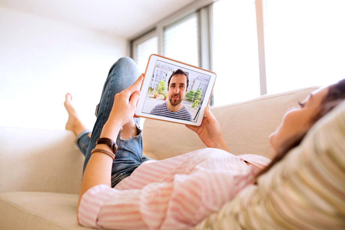 Egy nő egy tableten beszél a férfival, akivel távkapcsolatban él, miközben egy kanapén fekszik.