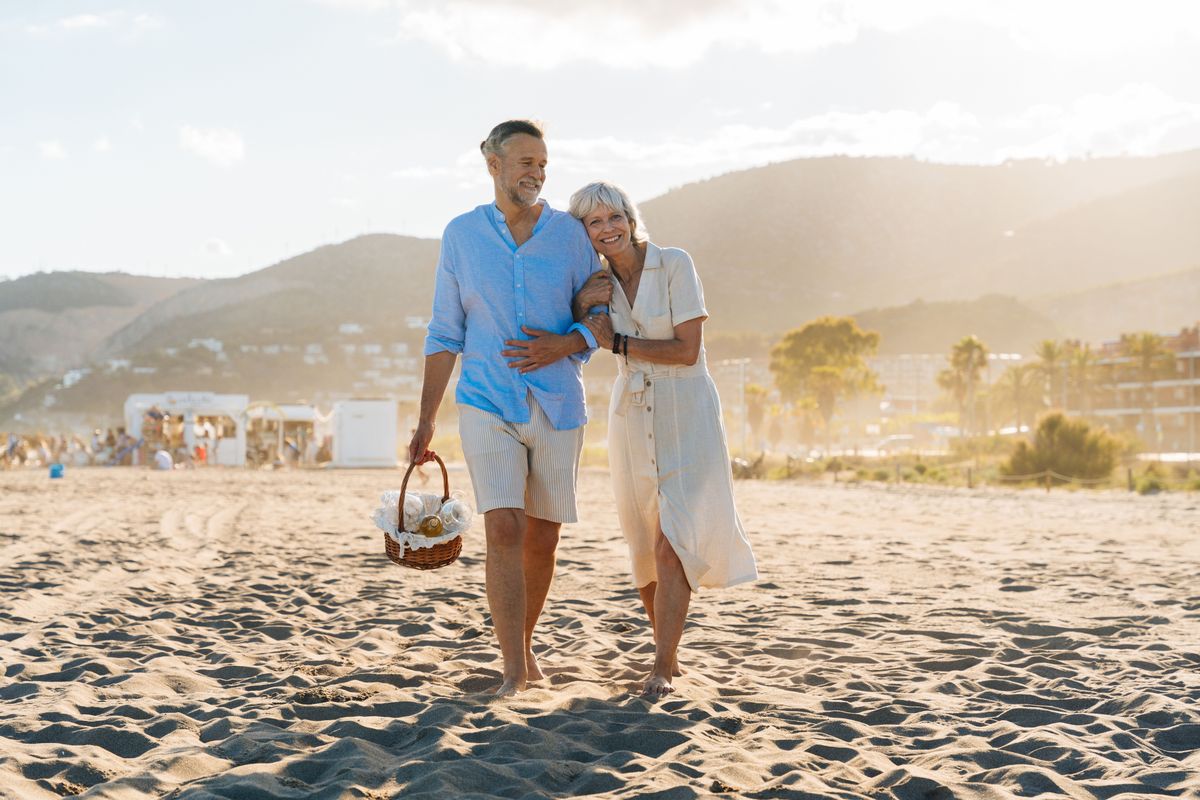 A vonzalom jele a férfiaknál: a mosoly, nevetés, figyelmesség, a közelség keresése, érdeklődés, gondoskodás, gyakori érintés.  Beautiful happy senior couple dating at the seaside during summertime - Mature married couple in love bonding outdoors at the beach, concepts about elderly lifestyle, relationship and quality of life