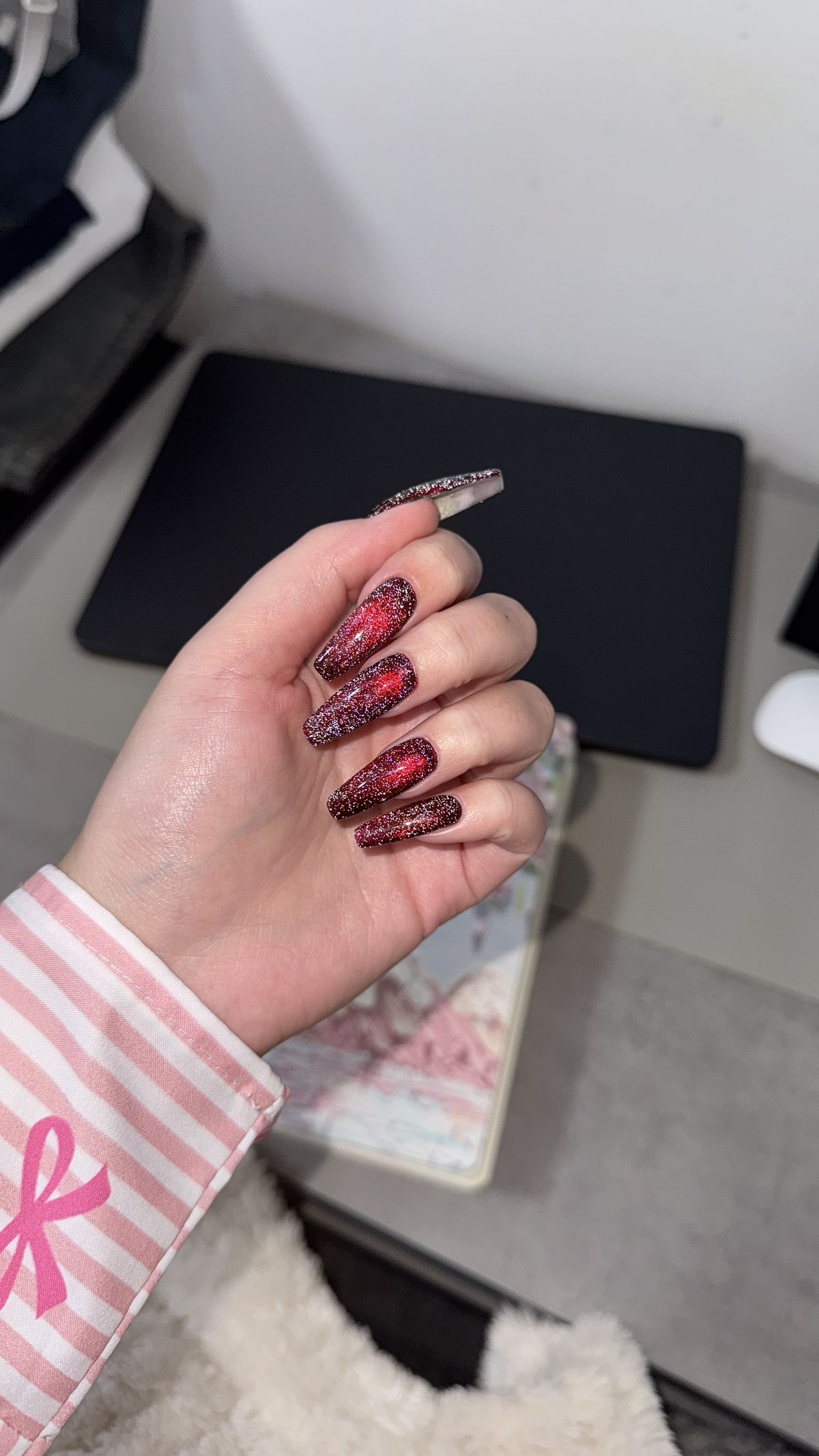 A hand with long, glittery red and black nails, showcasing an elegant and sparkly manicure.