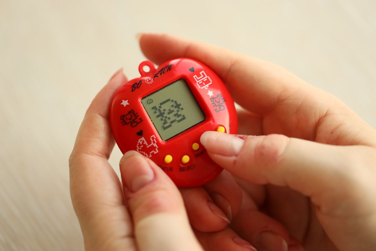 KYIV, UKRAINE - MARCH 9, 2024 Retro pet keychain game tamagotchi in red plastic case in female hands close up