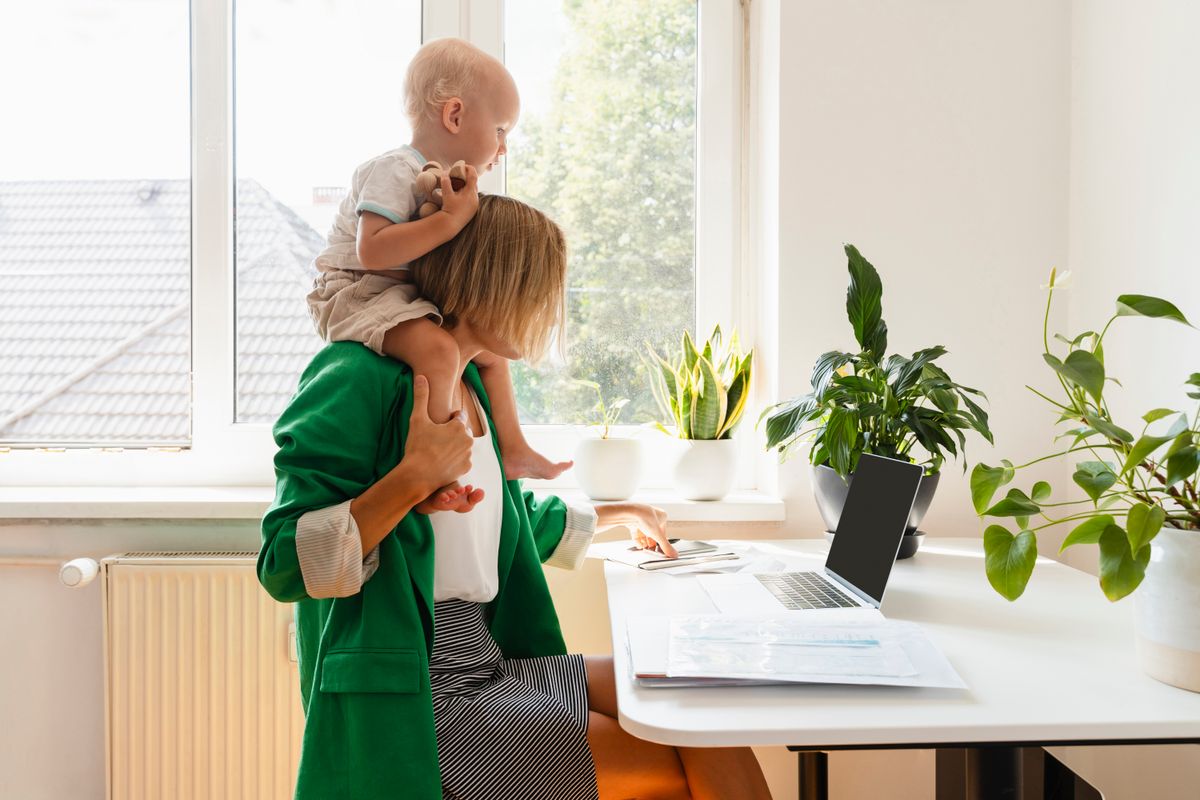 Egy nő multitasking közben a gyerekkel a nyakában laptopozik, ezzel rombolja az agy egészségét. 