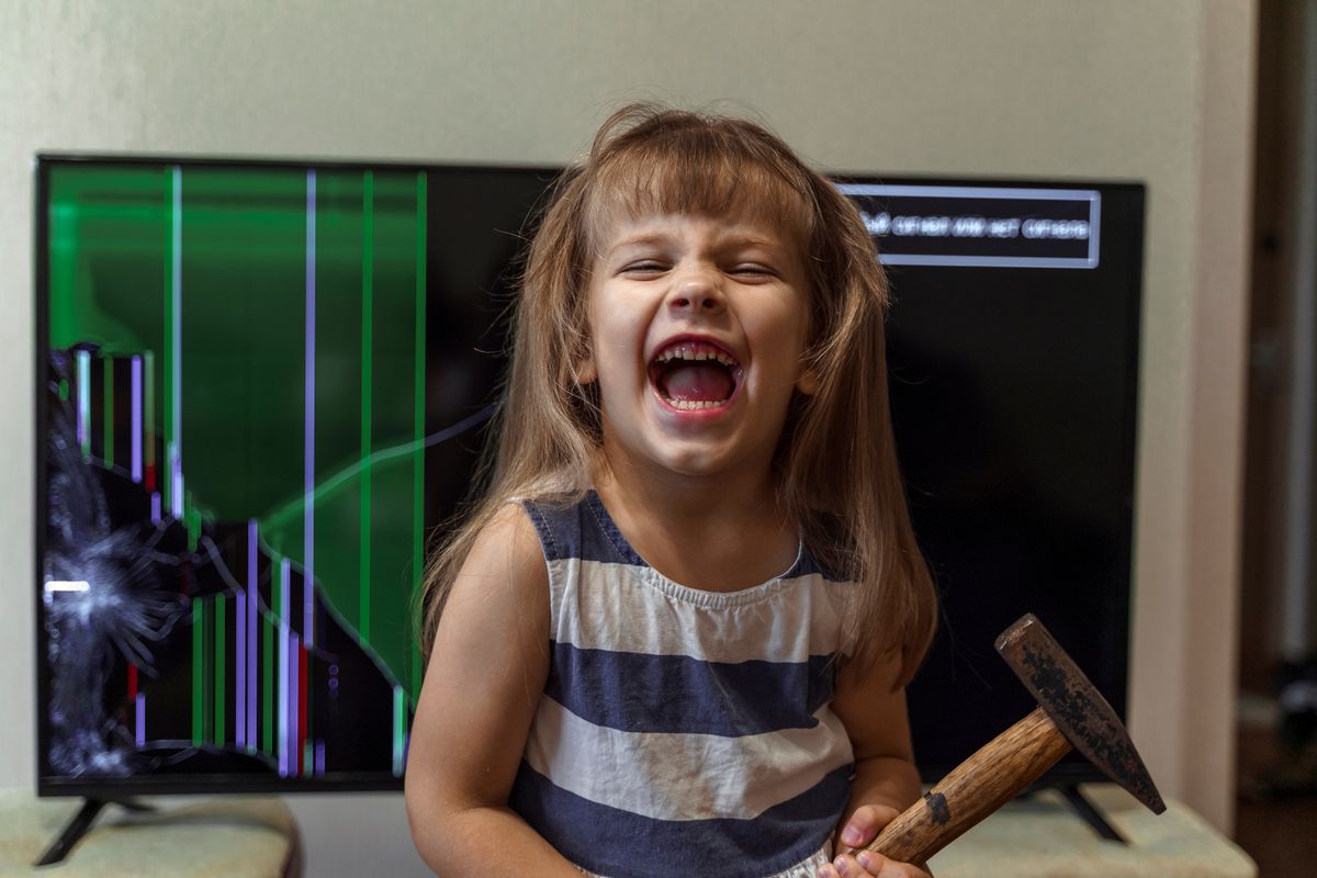 Stresszes gyerek: Mérges kislány kalpáccsal a kezében egy sérült TV előtt.