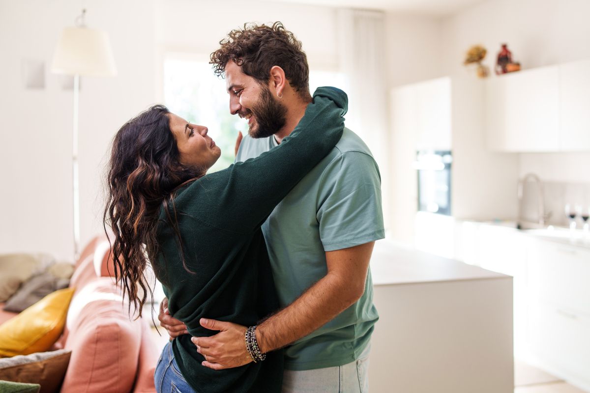 Relocation concept. A smiling cheerful multiracial couple in embraces lookin in each other eyes standing in the new apartment bought real estate, newlyweds get a mortgage
