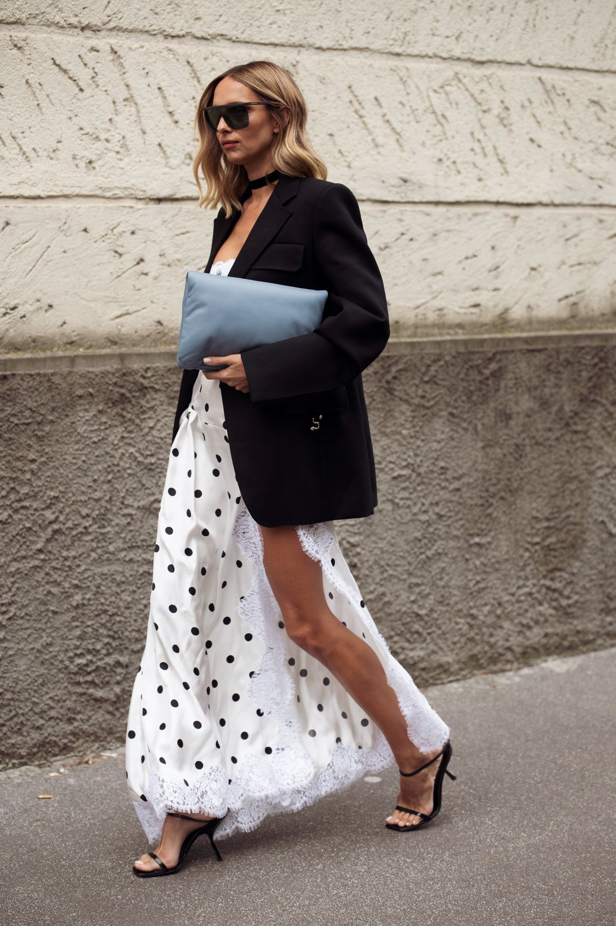 MILAN, ITALY - SEPTEMBER 26: Candela Pelizza wears a black oversized blazer over a white polka-dot slit dress with lace trim, styled with strappy heels, black sunglasses, and a blue clutch outside Sportmax show during the Milan Fashion Week Menswear Spring/Summer 2026 on September 26, 2025 in Milan, Italy. (Photo by Raimonda Kulikauskiene/Getty Images)