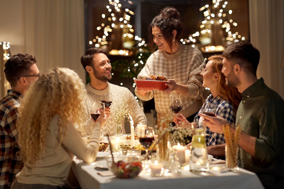 holidays, celebration and people concept - happy smiling friends having christmas dinner at home in evening