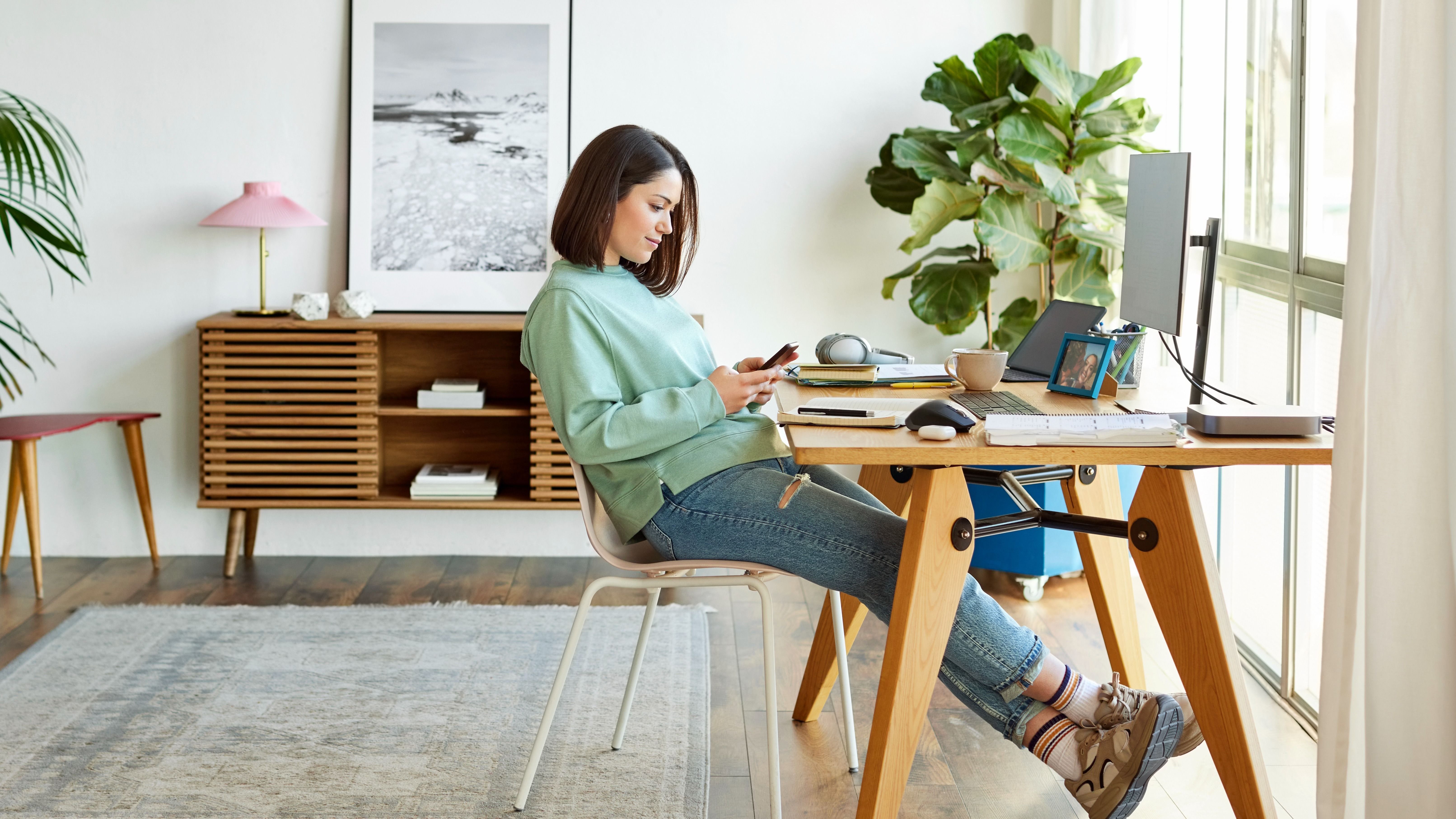 Egy nő home officeban a telefonját nyomkodja. 