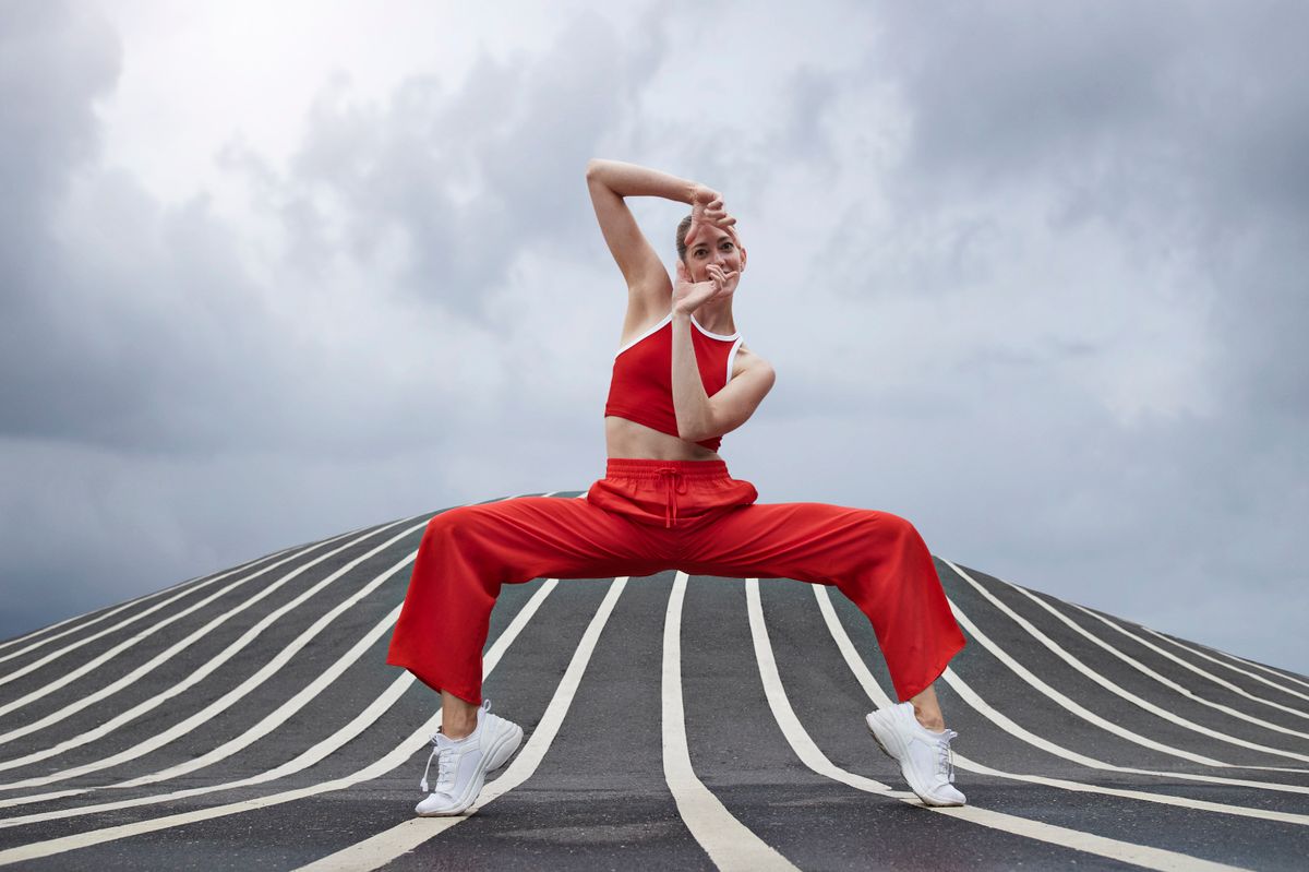 Mid adult female dancer gesturing while practicing dance on striped road against sky