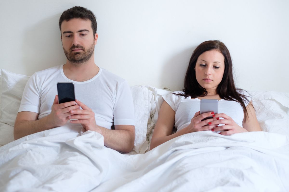 Egy pár az ágyban fekve unottan nyomogatja a telefonját, pedig szextingelhetnének is.