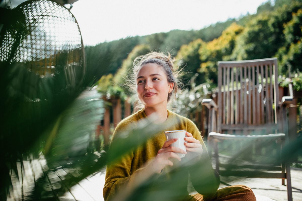 Woman with morning cup of coffee, sitting on patio and enjoying moment for herself. Portrait of beautiful woman.
