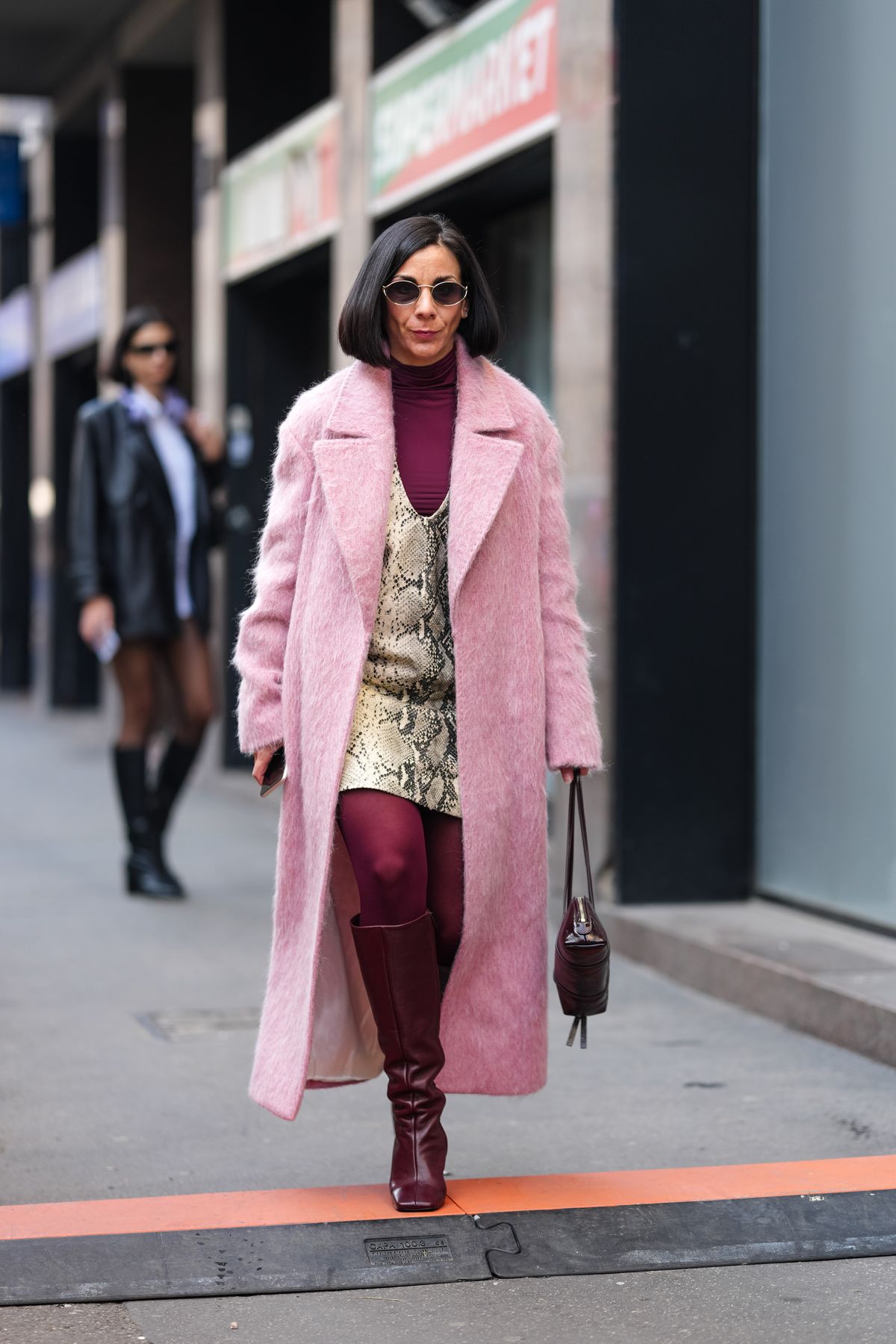 MILAN, ITALY - FEBRUARY 27: A guest wears dark brown bob, black sunglasses, burgundy bordeaux turtleneck long sleeve shirt, light gray python snakeskin pattern/print mini dress, light pink faux fur coat, burgundy bordeaux tights, shiny burgundy bordeaux knee high heeled boots leather shoes, outside Blumarine, during the Milan Fashion week Women's Fall/Winter 2025-2026 on February 27, 2025 in Milan, Italy. (Photo by Edward Berthelot/Getty Images)