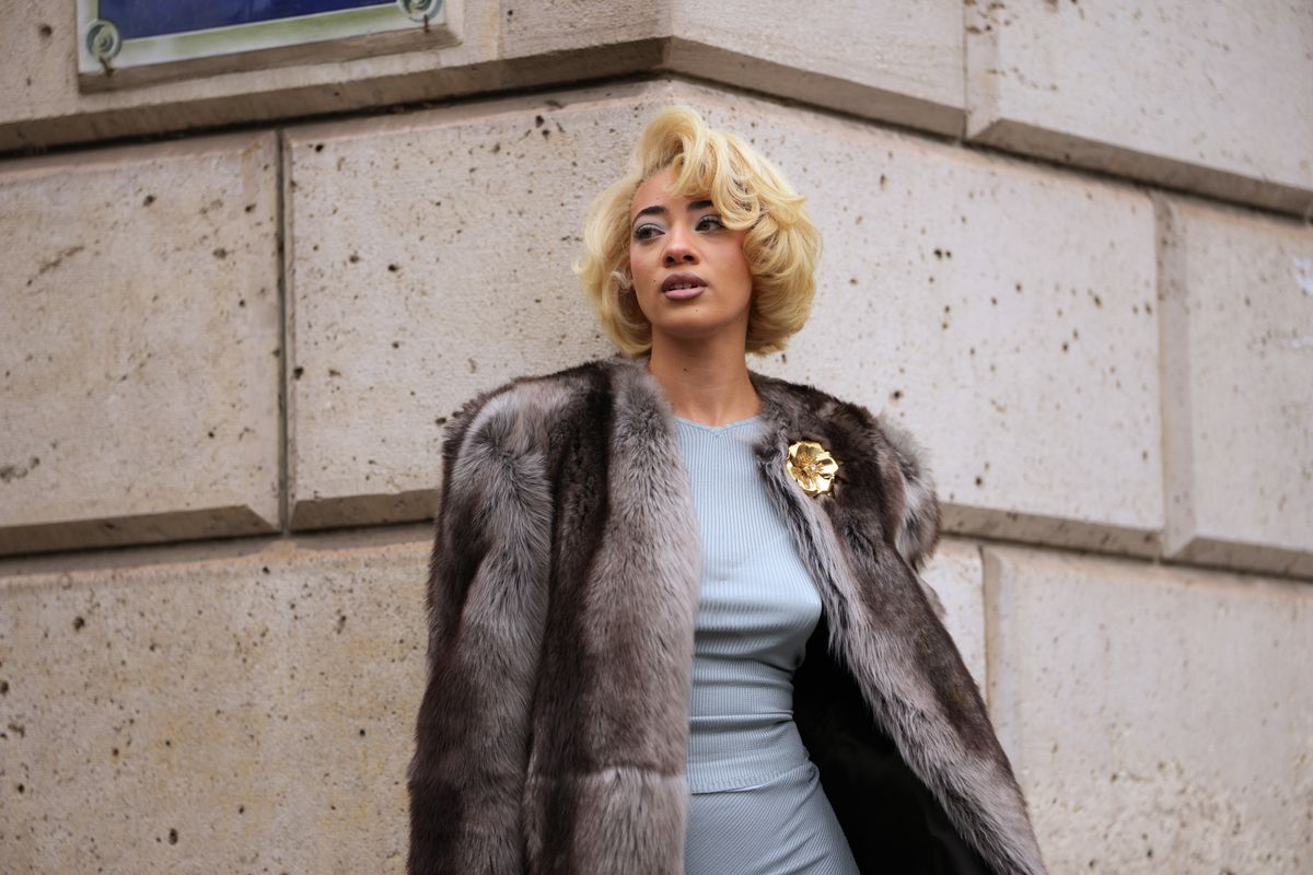 PARIS, FRANCE - OCTOBER 06: Reign Judge wears a short platinum-blonde waved bob with a side part, a gold metal floral brooch, a brown and grey fur coat, a pale blue ribbed knit fitted dress with crew neckline and knee-grazing hem, outside Miu Miu, during Paris Fashion Week - Womenswear Spring Summer 2026, on October 06, 2025 in Paris, France (Photo by Edward Berthelot/Getty Images)